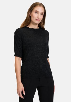 Pull à manches courtes noir avec une finition texturée et brillante, et un col à volants, associé à un pantalon noir. Design simple et ajusté.