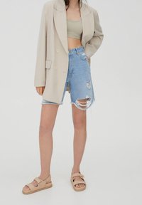 Beige oversized blazer, světle zelený cropped top, zničené světle modré džíny s třepeným lemem a taupe sandály se stuhami.