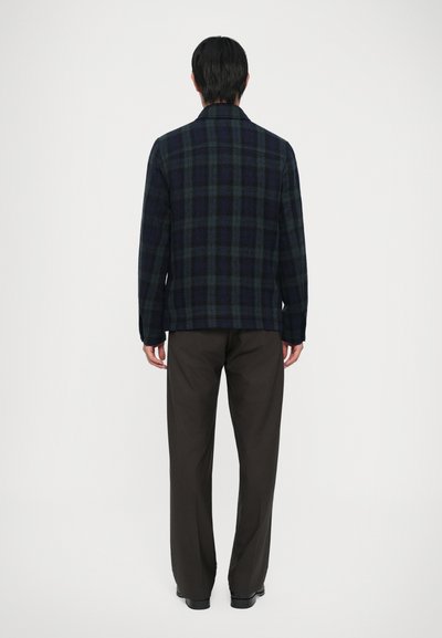 Camicia in flanella di colore blu scuro con motivo scozzese verde, dotata di colletto e maniche lunghe, abbinata a pantaloni scuri.