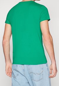 Zielona koszulka z okrągłym dekoltem, wykonana z bawełny, z krótkimi rękawami, gładką fakturą i prostym, dopasowanym krojem.