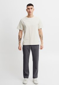 Jasnoszara bawełniana koszulka z krótkimi rękawami w połączeniu z ciemnoszarymi spodniami typu slim fit i białymi sneakersami. Prosty, swobodny zestaw bez wzorów.