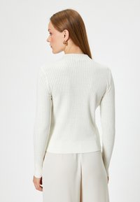Weißer gerippter Strickpullover mit langen Ärmeln und tailliertem Design, mit einem dezenten hohen Ausschnitt und einer weichen, strukturierten Oberfläche.