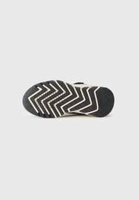 Suola di scarpa atletica nera con un motivo a zigzag e accenti beige. Presenta un materiale in gomma testurizzata per aderenza e durata.