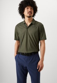 Short-sleeve olive green polo shirt with textured pattern; paired with navy blue pants and black woven belt, featuring a subtle logo on the chest.
