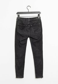 Jeans skinny de denim negro con cintura alta, bolsillos traseros y detalles de costura visibles en las piernas, colgados de una percha negra.