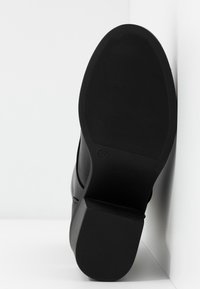 Semelle en caoutchouc noir d'une chaussure avec une surface texturée et un léger talon, dotée d'un bout arrondi et de détails de style minimaux. Taille marquée comme 37.
