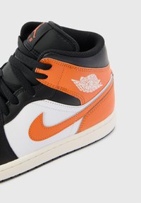 Black, white, and orange leather sneaker with a high-top design, featuring a prominent Nike swoosh, and textured detailing on the tongue.