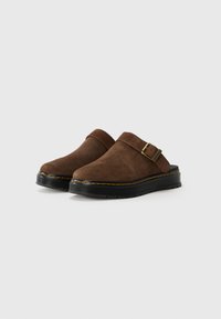 Zoccoli in suede marrone con suola piatta in gomma nera, dotati di un fermo laterale e cuciture gialle a contrasto lungo il bordo della suola.