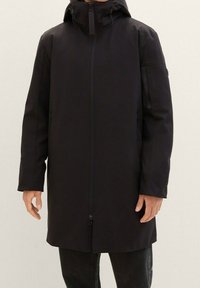 Black waterproof parka with a hood, full front zipper, and side pockets. Features a smooth texture and a slightly longer cut.