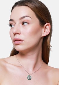 Collana d'argento con un pendente ovale caratterizzato da un motivo centrale, contornato da accenti verdi; catena delicata e superficie liscia.