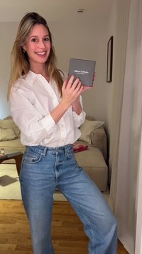 Gray box with "Marc O'Polo" text, held by a person in a white button-up shirt and blue jeans, set in a beige interior.