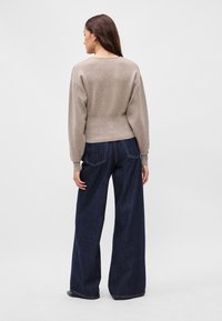 Μπεζ πλεκτό πουλόβερ με στρογγυλή λαιμόκοψη, συνδυασμένο με σκούρα μπλε τζιν παντελόνι φαρδιάς γραμμής με εμφανή ραφή και χαλαρή εφαρμογή.