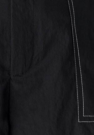 Crna tkanina s kontrastnim bijelim šavovima koji ocrtavaju pravokutni oblik i detaljima zakrivljenog šava na teksturiranom materijalu.