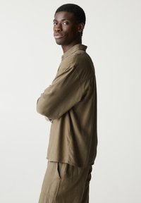 Cămașă ușoară de culoare verde măslină, cu croi relaxat, guler și mâneci lungi, asortată cu pantaloni tapered. Design simplu, textură moale.