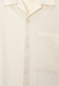 Camicia bianca con bottoni in tessuto testurizzato. Presenta una tasca sul lato sinistro e un colletto classico, completata da bottoni in plastica.
