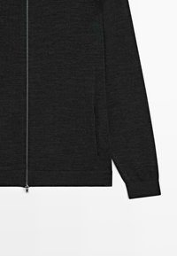 Maglione nero con zip e maniche lunghe, realizzato in tessuto texturizzato. Presenta due tasche laterali e polsini e orlo a coste.
