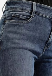 Ciemnoniebieskie dżinsy o dopasowanym kroju, z tylną kieszenią, delikatnym przecieranym wyglądem oraz żółtym przeszyciem wzdłuż szwów.