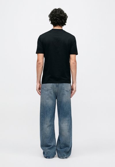 Μαύρο κοντομάνικο μπλουζ�άκι συνδυασμένο με φαρδιά, ξεθωριασμένα μπλε τζιν παντελόνια. Το ντύσιμο έχει άνετη εφαρμογή και απλό σχέδιο.