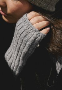 Grijze geribbelde gebreide trui met glinsterende draden, voorzien van een duimgat en een gestructureerde afwerking, getoond tegen een donkere achtergrond.