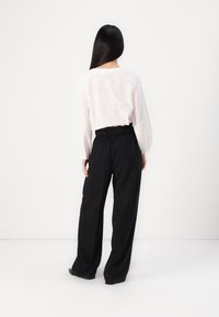 Camisa blanca de manga larga con bordado texturizado, combinada con pantalones de pierna ancha negros de talle alto que tienen cintura elástica y bolsillos.