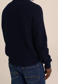 Marinblå stickad tröja med en texturerad, ribbad design. Har en rund halsringning och en något oversized passform, tillsammans med denimjeans.