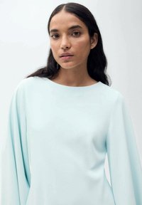 Svetlo modra, bluza z dolgimi rokavi in okroglim izrezom ter gladko teksturo. Ima sproščene rokave in minimalističen dizajn.