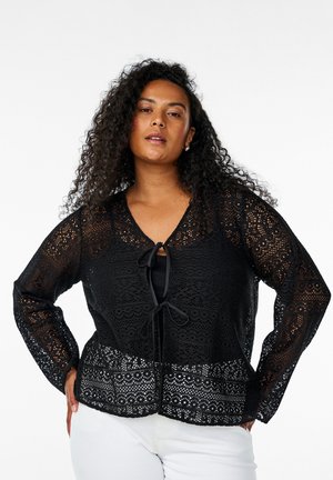 Black lace blouse with a v-neckline, long sleeves, and tie detail at the front. Features intricate patterns and a slightly loose fit.