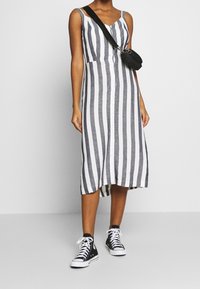 Pruhované bezramínkové šaty v šedé a bílé barvě s knoflíkovou přední částí a midi délkou, spárované s černými vysokými teniskami. Taška s nastavitelným popruhem.