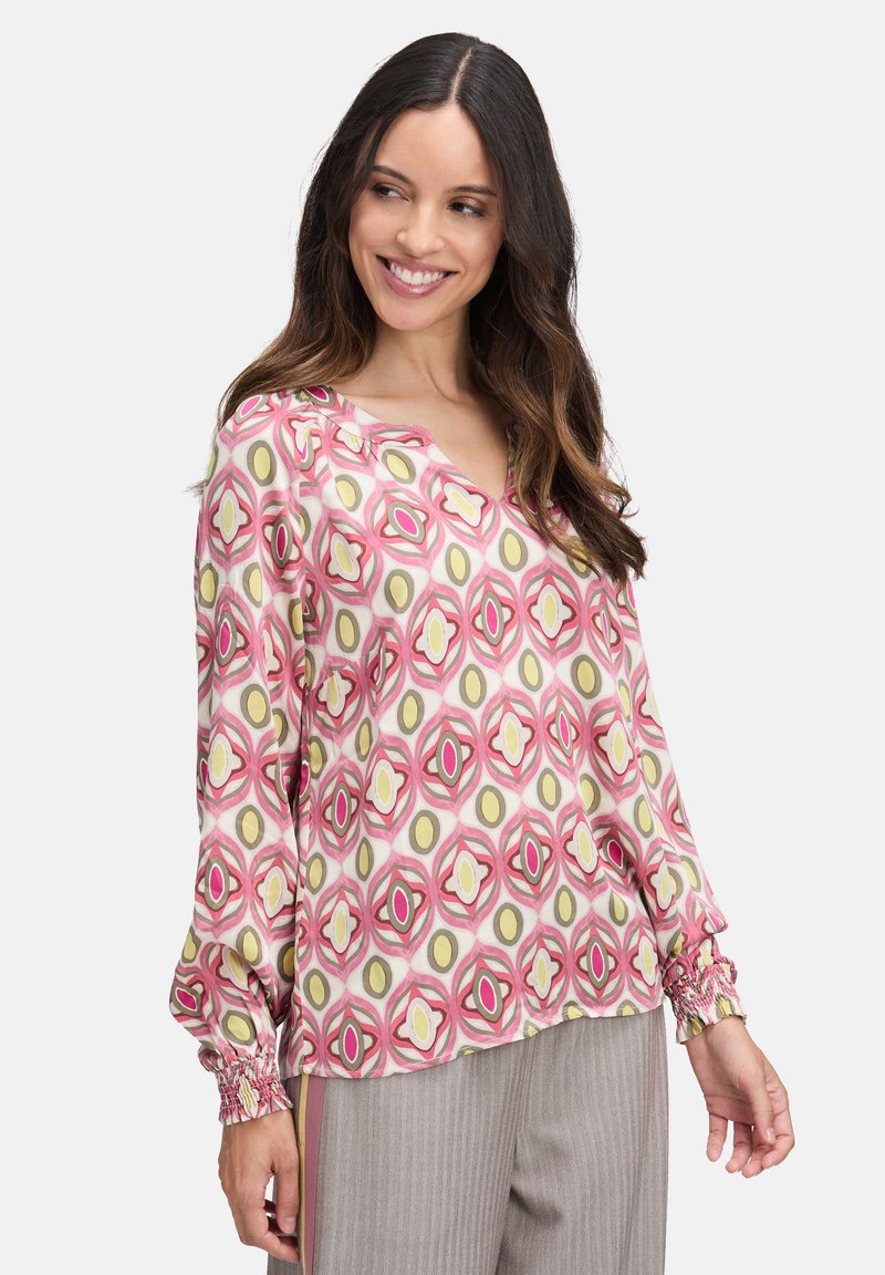 Langärmlige Bluse mit einem auffälligen geometrischen Muster in Rosa, Gelb und Grün. V-Ausschnitt-Design mit gerüschten Bündchen und leichtem Stoff.