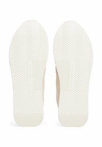 Sneaker beige con suole in gomma piatta caratterizzate da un motivo a spina di pesce. La suola presenta dettagli del marchio in rilievo e una finitura opaca liscia.