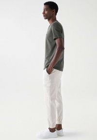 Graues T-Shirt, locker sitzende weiße Cargo-Hosen mit elastischen Bündchen und weiße Sneaker. Einfaches Design mit Taschen an den Hosen.