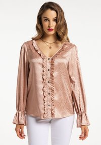 Camicia rosa chiaro con ruffles in tessuto lucido e motivo testurizzato. Presenta un collo a V, chiusura con bottoni frontale e maniche a campana.