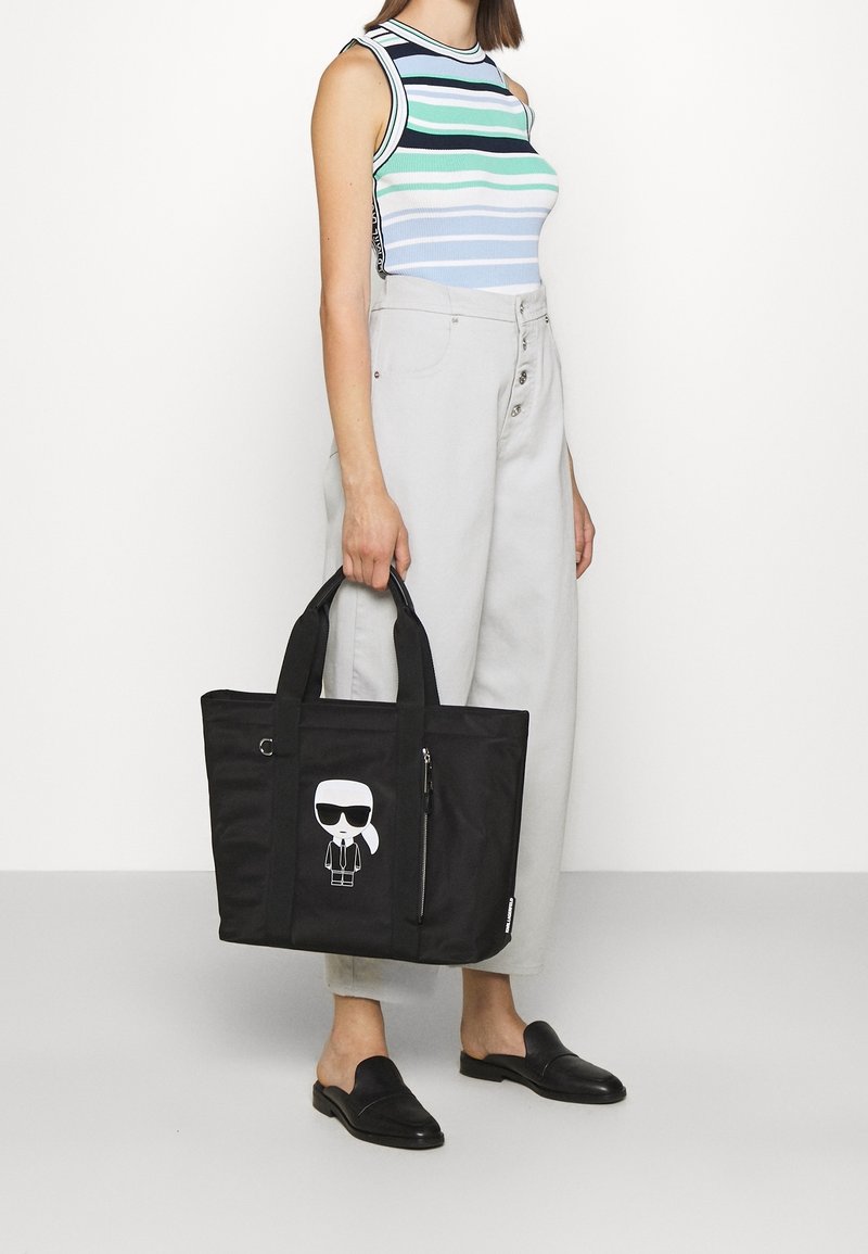 Zwarte schoudertas van duurzame stof, met een cartoonafbeelding, een ritsvak en dubbele handvatten. Stevig, gestructureerd ontwerp.