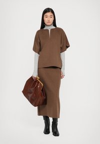 Brown wool top with short sleeves and a keyhole neck, paired with a matching brown skirt. Holding a glossy brown bag. Black knee-high boots.