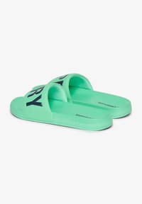 Lichtgroene slip-ons met twee brede banden met daarop donkere tekst. Glad oppervlak en platte zool, merk met "SUPERDRY" aan de zijkant.