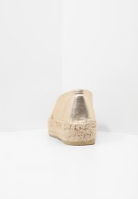 Espadrillas metallizzate in oro con suola in juta intrecciata, retro arrotondato, texture liscia, design slip-on e dettagli minimi.