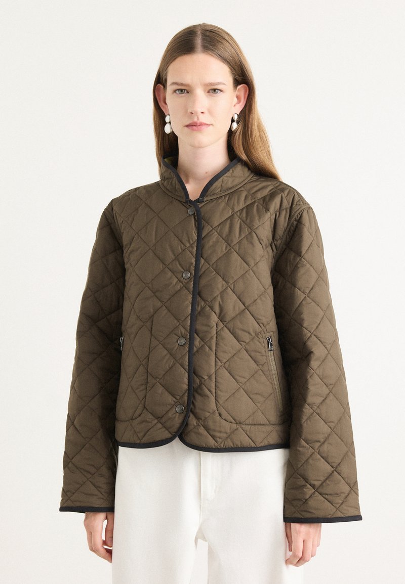Veste matelassée marron avec un col arrondi, des bordures noires, des boutons-pression et des poches latérales. Le matériau semble rembourré avec une texture lisse.
