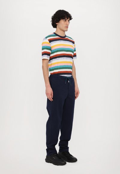Tricou striped din bumbac multicolor cu mâneci scurte, asociat cu pantaloni elastici bleumarin și adidași negri. Textură plată și netedă.