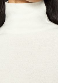 Sweter z wysokim kołnierzem, prążkowany z miękkiej białej dzianiny, z dopasowanym krojem i teksturalnym wykończeniem, w minimalistycznym stylu.