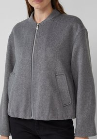 Veste bomber grise en mélange de laine douce, avec un col montant, une fermeture éclair sur le devant et des poches latérales, offrant une coupe décontractée.