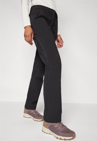 Svarta utomhusbyxor med slim fit, dragkedjefickor och en jämn textur. I kombination med ljuslila träningssandaler.