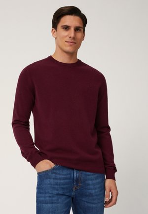 Maglione borgogna a maglia con collo rotondo e maniche lunghe, realizzato in un tessuto morbido. Abbinato a jeans in denim blu.