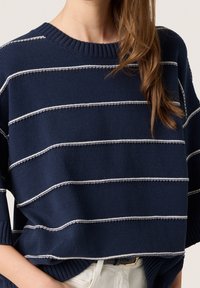 Dunkelblauer Strickpullover mit weißen horizontalen Streifen, geribbtem Ausschnitt und weiten Ärmeln, mit lockerem Sitz und strukturiertem Stoff.
