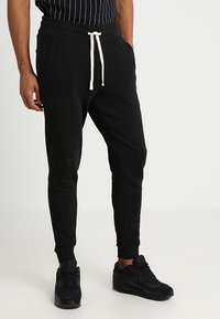 Black jogger pants made from cotton, featuring a drawstring waist in cream, fitted cuffs, and a smooth texture.