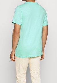 Tyrkysový crew-neck tričko vyrobené z měkké bavlny, s krátkými rukávy a rovný střih. Viditelné švy podél lemů a rukávů.