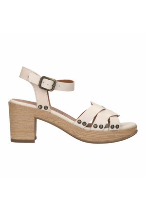 Beige leather sandal with a chunky wooden heel, featuring wide crossed straps, metal studs, and an adjustable ankle strap.