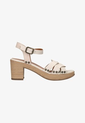 Beige leren sandaal met een chunky houten hak, voorzien van brede gekruiste banden, metalen studs en een verstelbare enkelband.