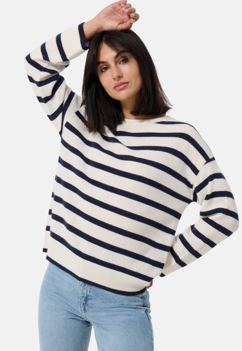 Sweter w paski w kolorze kremowym i granatowym, wykonany z miękkiej tkaniny, z okrągłym dekoltem i opadającymi ramionami, w połączeniu z jasnoniebieskimi dżinsami.