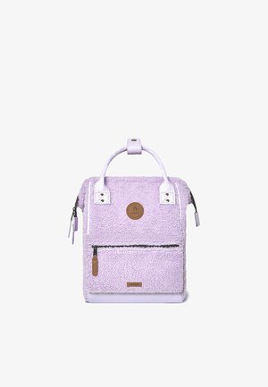 Purple plush backpack with faux fur texture, leather accents, top handle, and a front zippered pocket. Features a round logo patch.