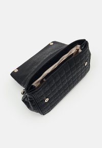 Mustan tekstuurin käsilaukku, jossa on tikattu muotoilu. Varustettu kultaisilla yksityiskohdilla, vetoketjullisella osastolla ja vaalealla sisävuorella. Auki oleva näkymä.